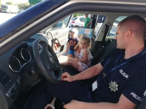 Policjant prezentuje dzieciom radiowóz podczas festyny charytatywnego.
